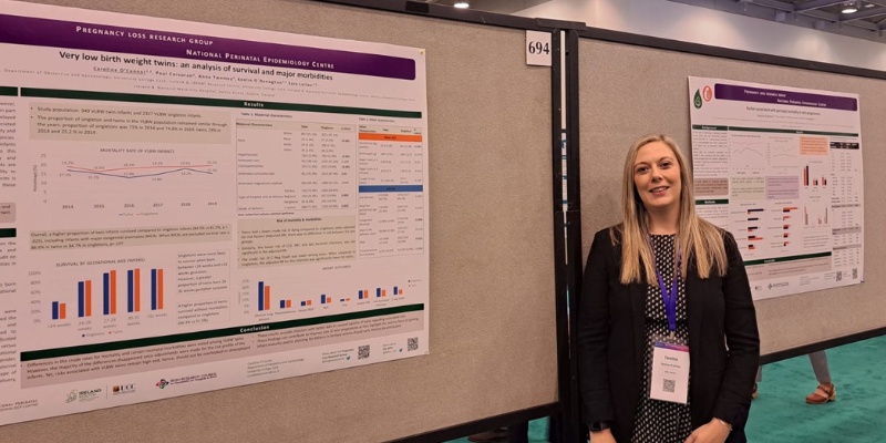 Woman with long blond hair wearing a lanyard standing in front of a large poster display