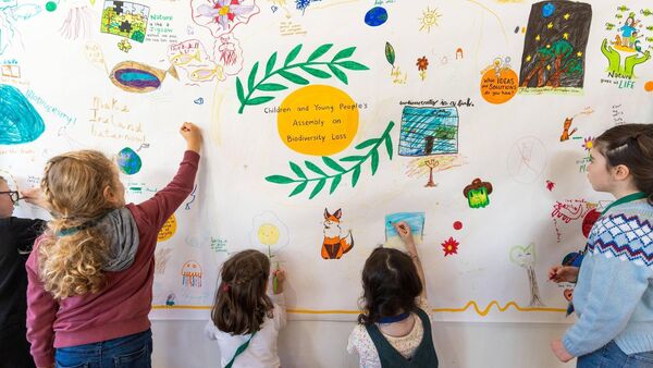 A small group of children draw pictures on a wall.