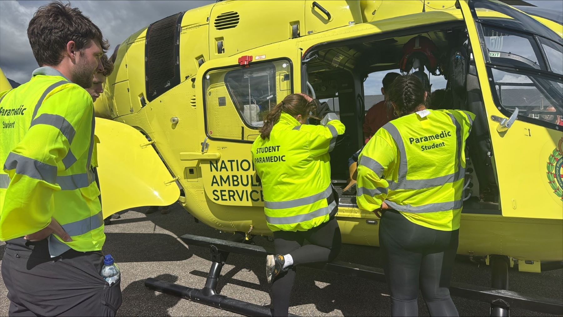 group of student apprentice paramedics gathered at a helicopter in hi-vis yellow gear