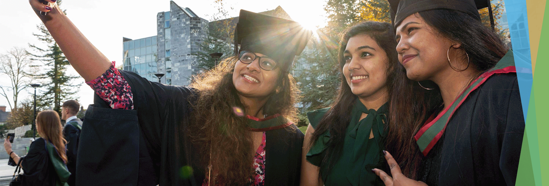 Three international students in graduation gowns taking a selfie on campus