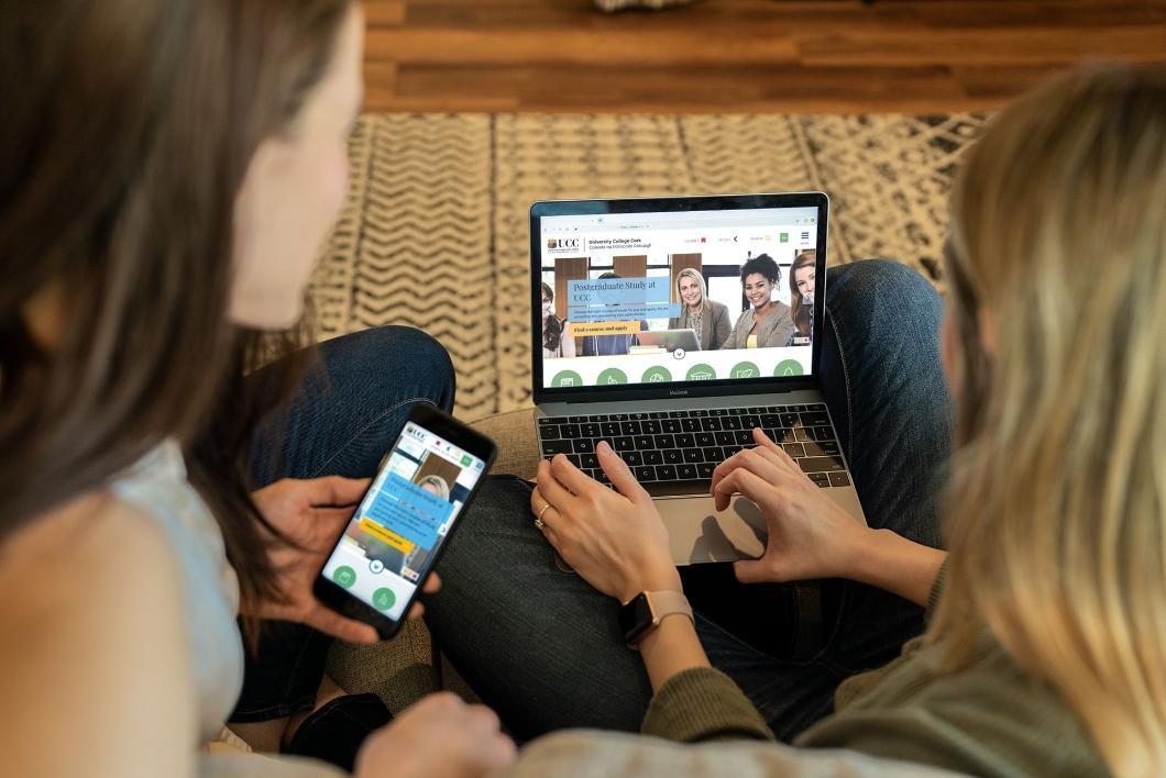 two women looking at the ucc homepage on a laptop and phone