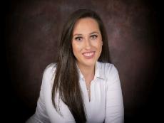 Headshot of student with long dark hair smiling for the camera. She wears a long sleeved white shirt open at the collar.