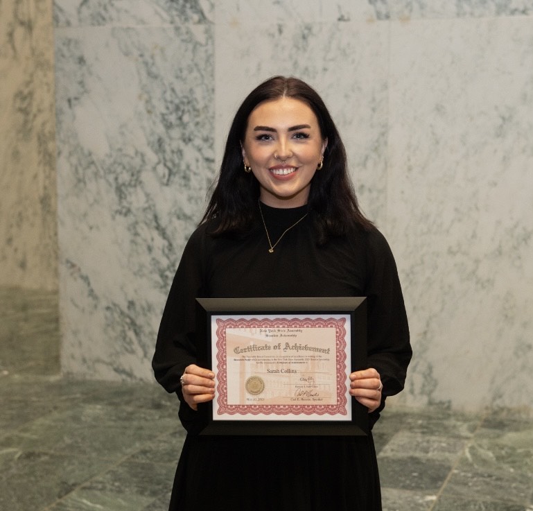 Smiling student with long dark hair holding up a certificate for the camera.