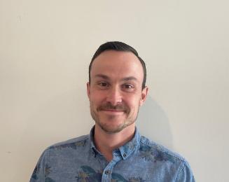 Headshot of smiling man in a blue shirt against a pale background.