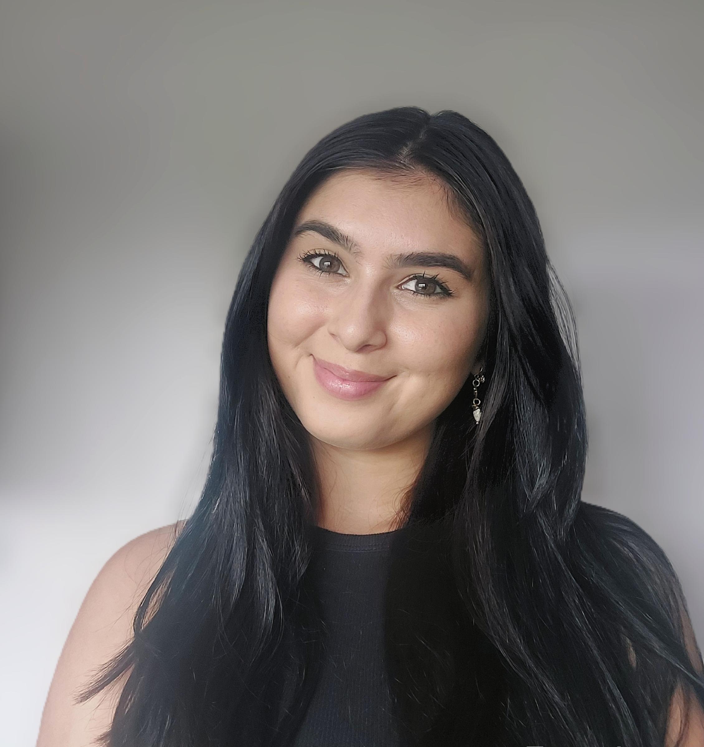 Headshot of student with long dark hair and a dark top smiling for the camera.