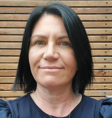 Headshot of dark-haired Irene, MBA student, wearing a navy top looking directly at the camera against a brown fence-type background.