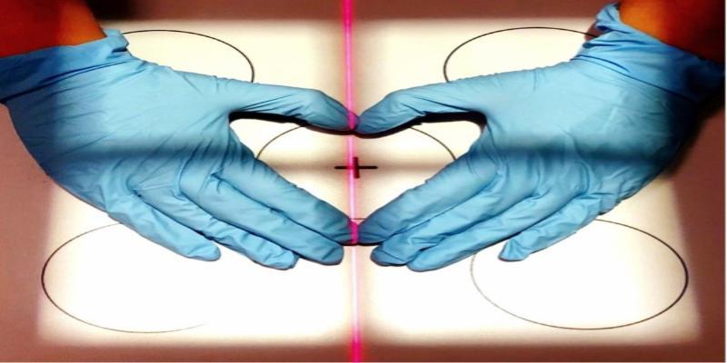 Hands in blue gloves making a heart-shaped image over a body marked up for a scan.