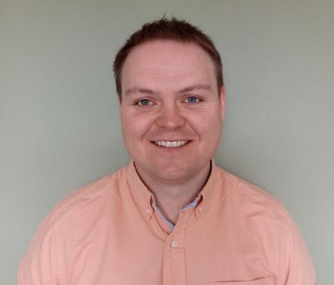 Headshot of smiling man wearing a pink shirt open at the collar.