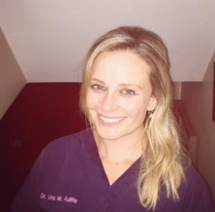 Woman in purple scrubs, with long fair hair, smiling broadly at the camera.