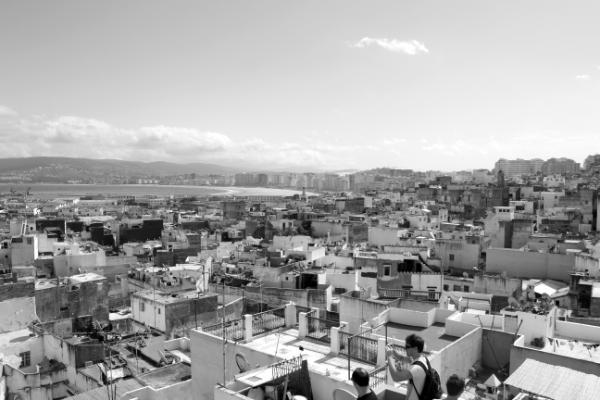 UNIC Black and white urban landscape of flat roofed houses in close proximity stretching out into the distance. The sea can be viewed in the distance.