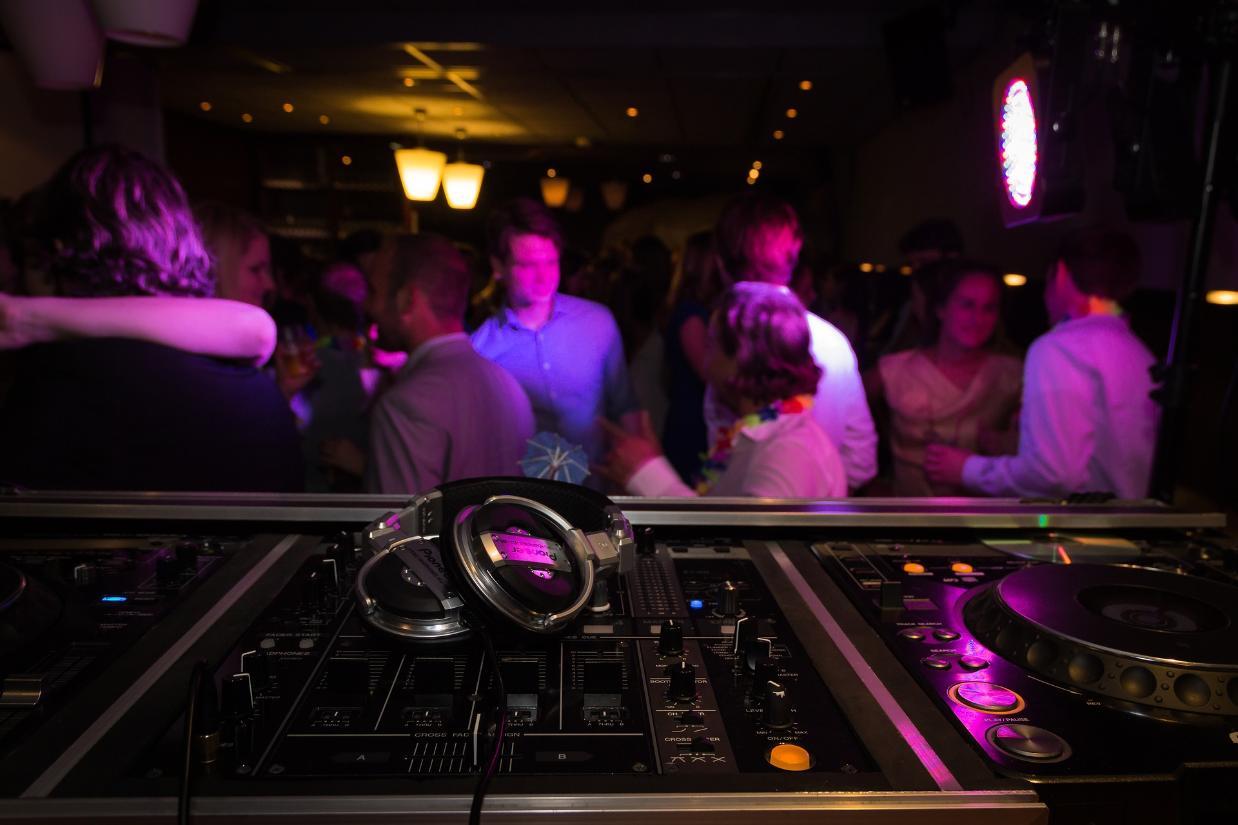 foreground of DJ's mixing desk with people dancing in the background out of focus