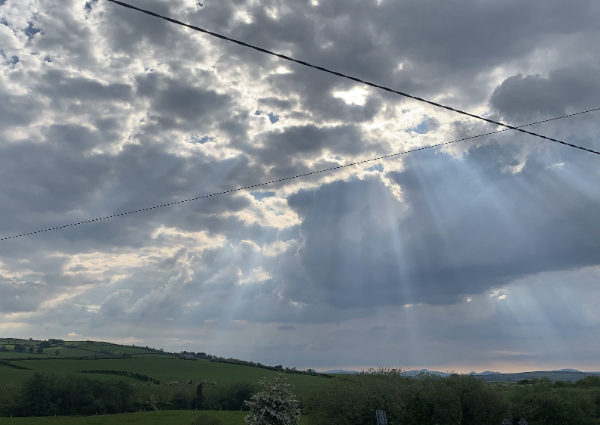 Photograph of the cloudy sky in the Irish countryside with streaks of sunlight breaking through