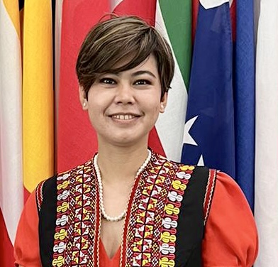 A smiling woman with short brown hair wearing an embroidered red jacket