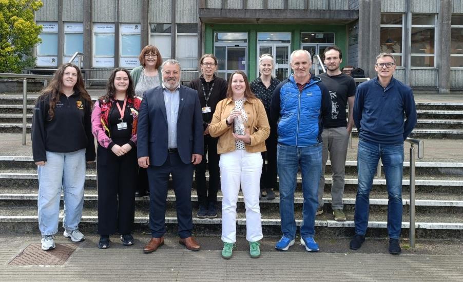 A group of people standing on the front steps of a building with one person holding an award.