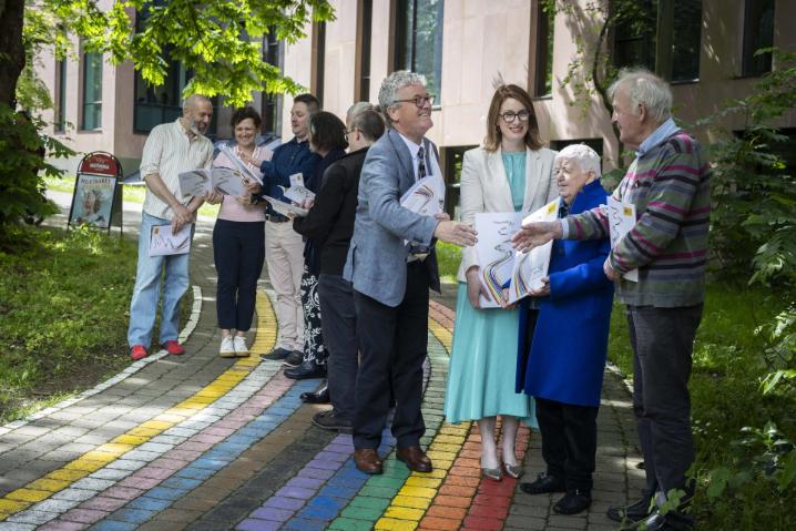 Two groups of people standing gathered on the Rainbow Walkway, greeting eachother, some are looking at a document together and smiling. Two groups of people standing gathered on the Rainbow Walkway, greeting eachother, some are looking at a document together and smiling.