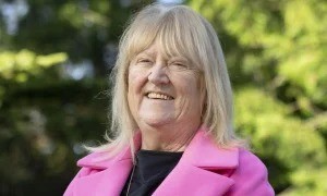 A smiling blonde woman in a pink jacket