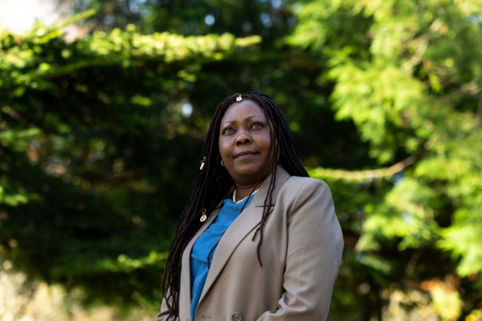 A woman with long dark hair and a beige jacket looking off into the distance