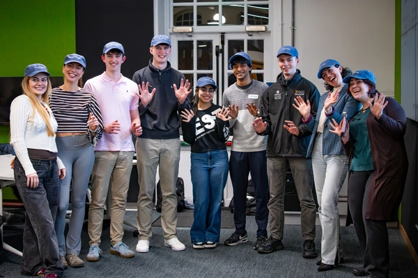 Group of 9 people wearing caps and smiling