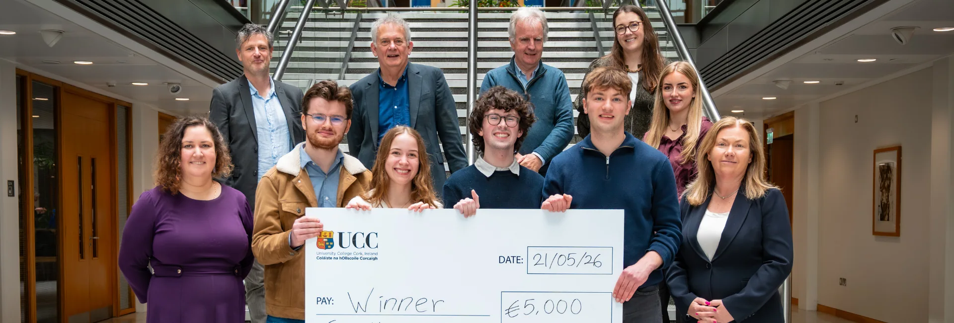 Image of 11 people smiling for a photo, a few in front are holding a check for 5000 euros
