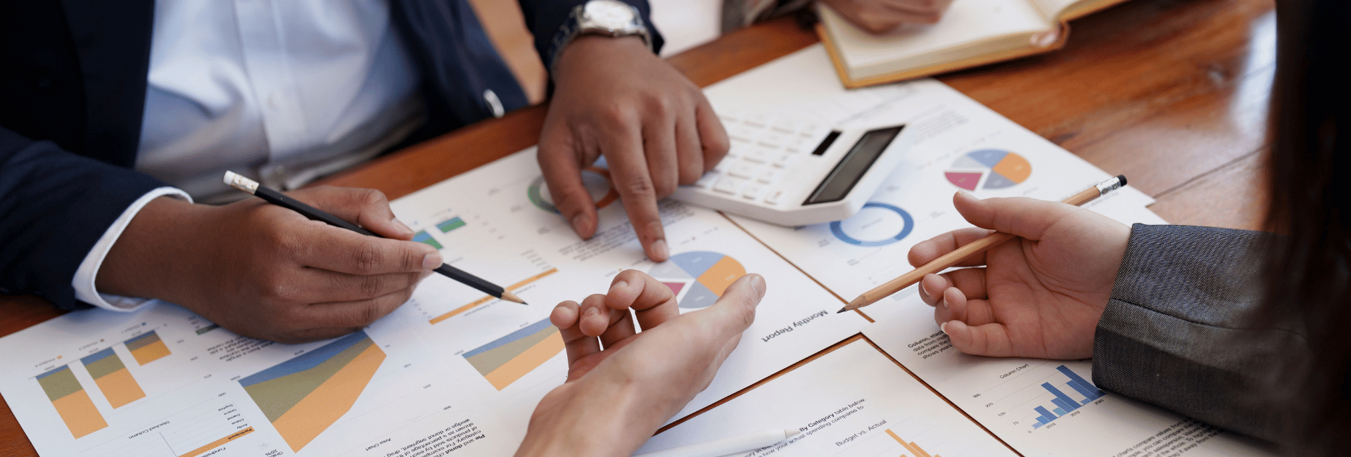 People in a business meeting with hands pointing at reports on table