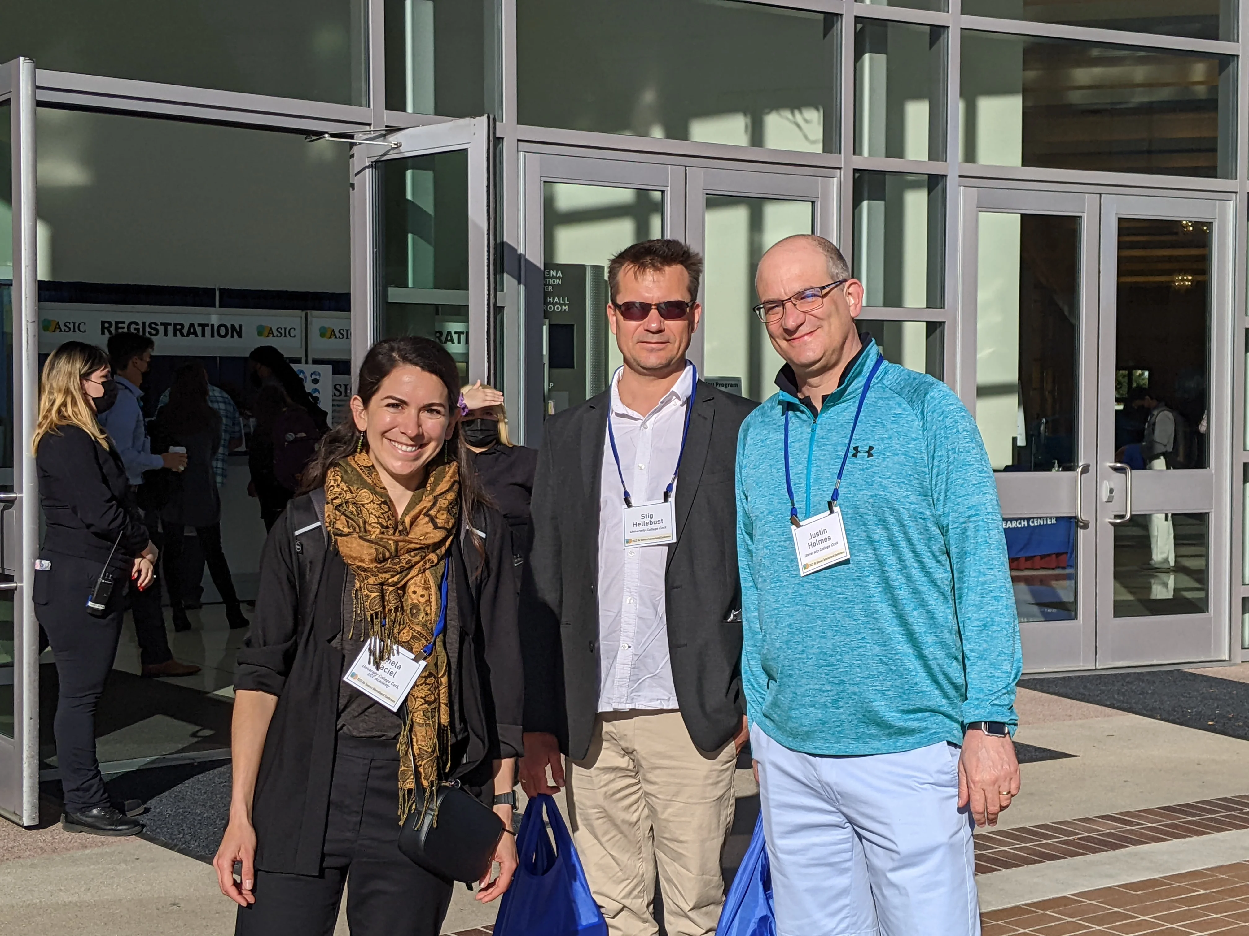 Three people standing together on a sunny day in front of a building