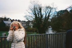 Girl posing on bridge with camera - grey clouds and a winter tree mark the bakground to this image.