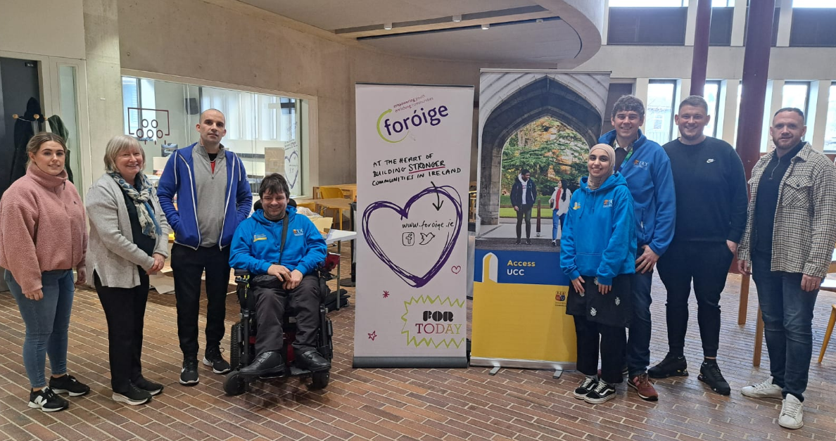 There are four people to the left and four to the right of 2 pop up stands for Access UCC and for Foroige. UCC staff and students in blue hoodies