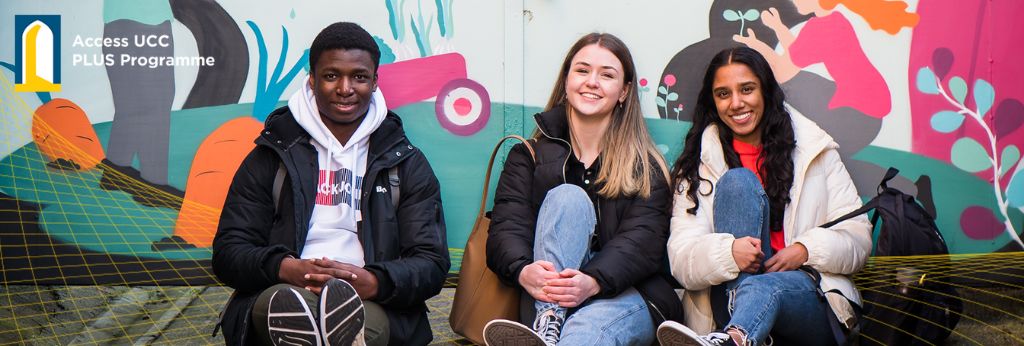 PLUS Programme Banner - Three students sitting by a colorful wall in UCC