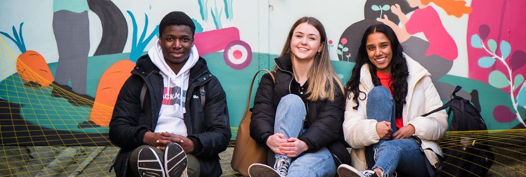 Access UCC Photoshoot - Three students sitting outside a wall by UCC