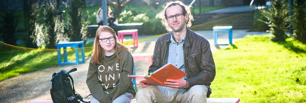 Access UCC Photoshoot - Two students sitting reading in the UCC QUAD