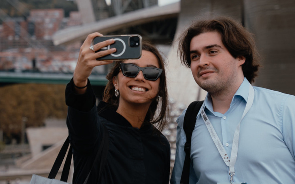 A young woman and young man pose for a selfie in front of the Guggenheim museum, Bilbao