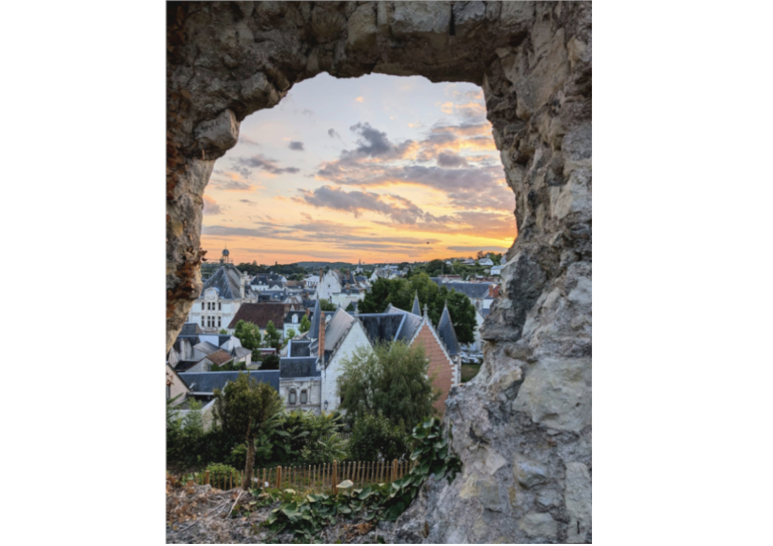 A historic French townscape is framed by a rock feature, with a sunset in the background